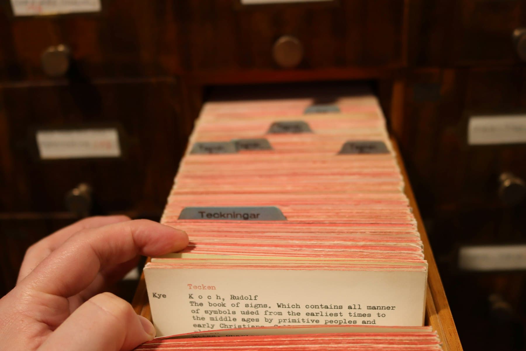 Eine Hand zieht eine Karteikarte aus einem historischen Bibliothekskatalog-Schrank