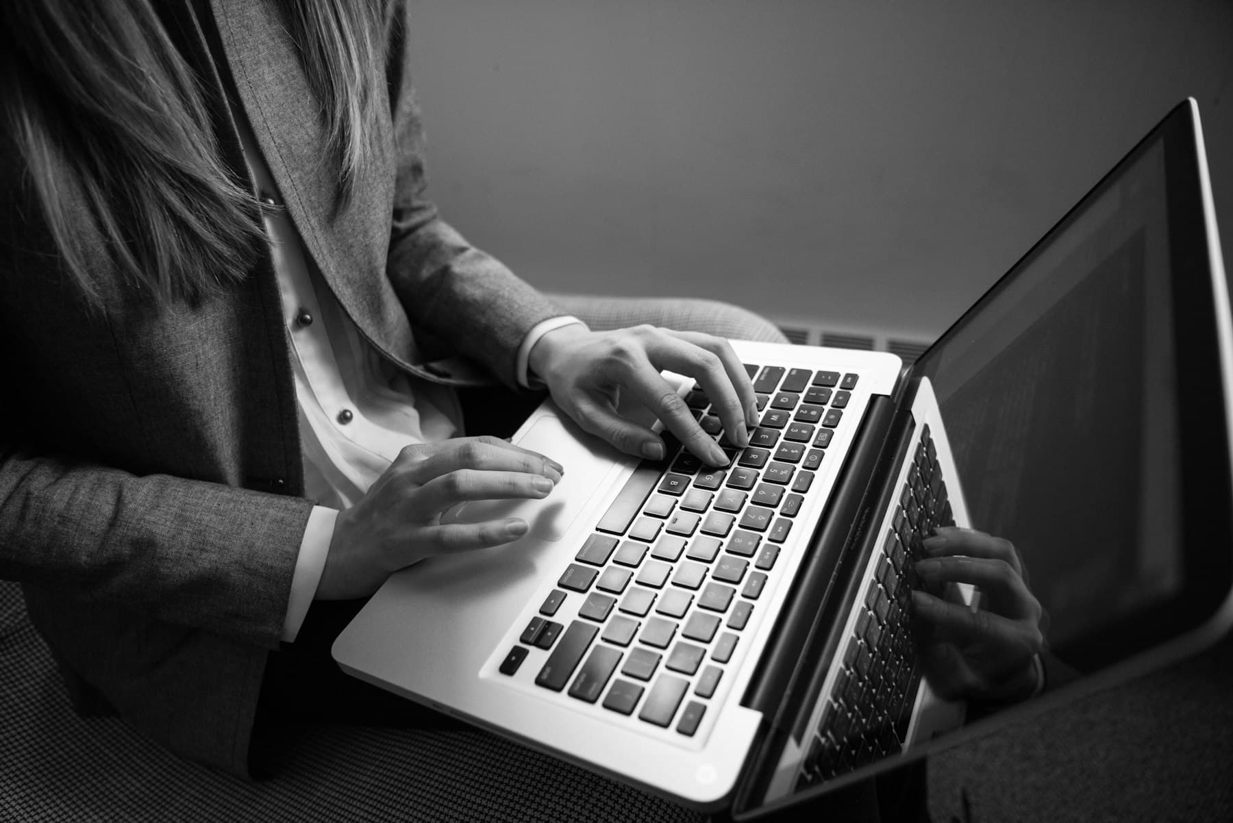 Schwarz-weiße Nahaufnahme von Händen, die konzentriert auf einer Laptop-Tastatur tippen