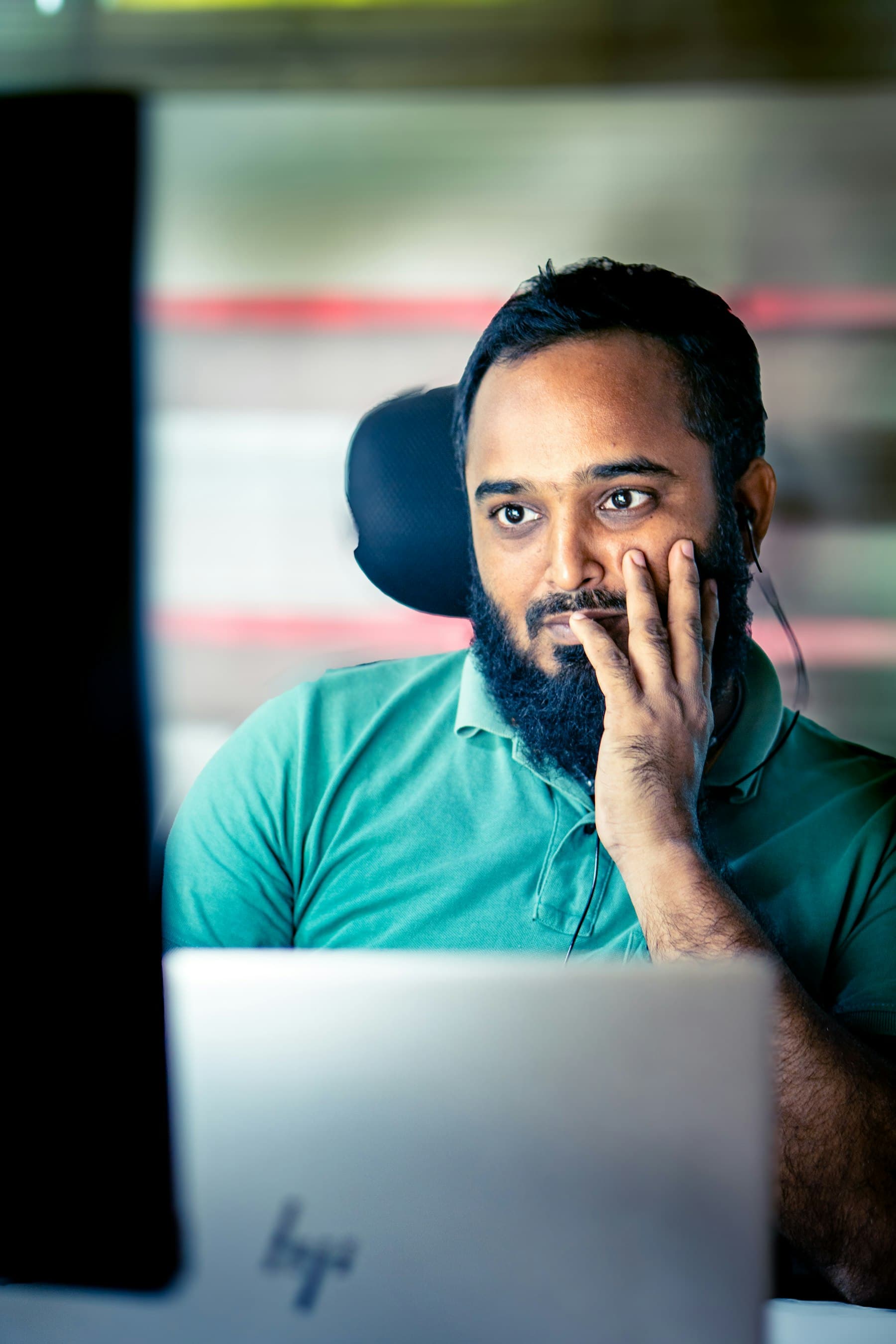 A man looks intently and thoughtfully at a screen, hand resting on his chin