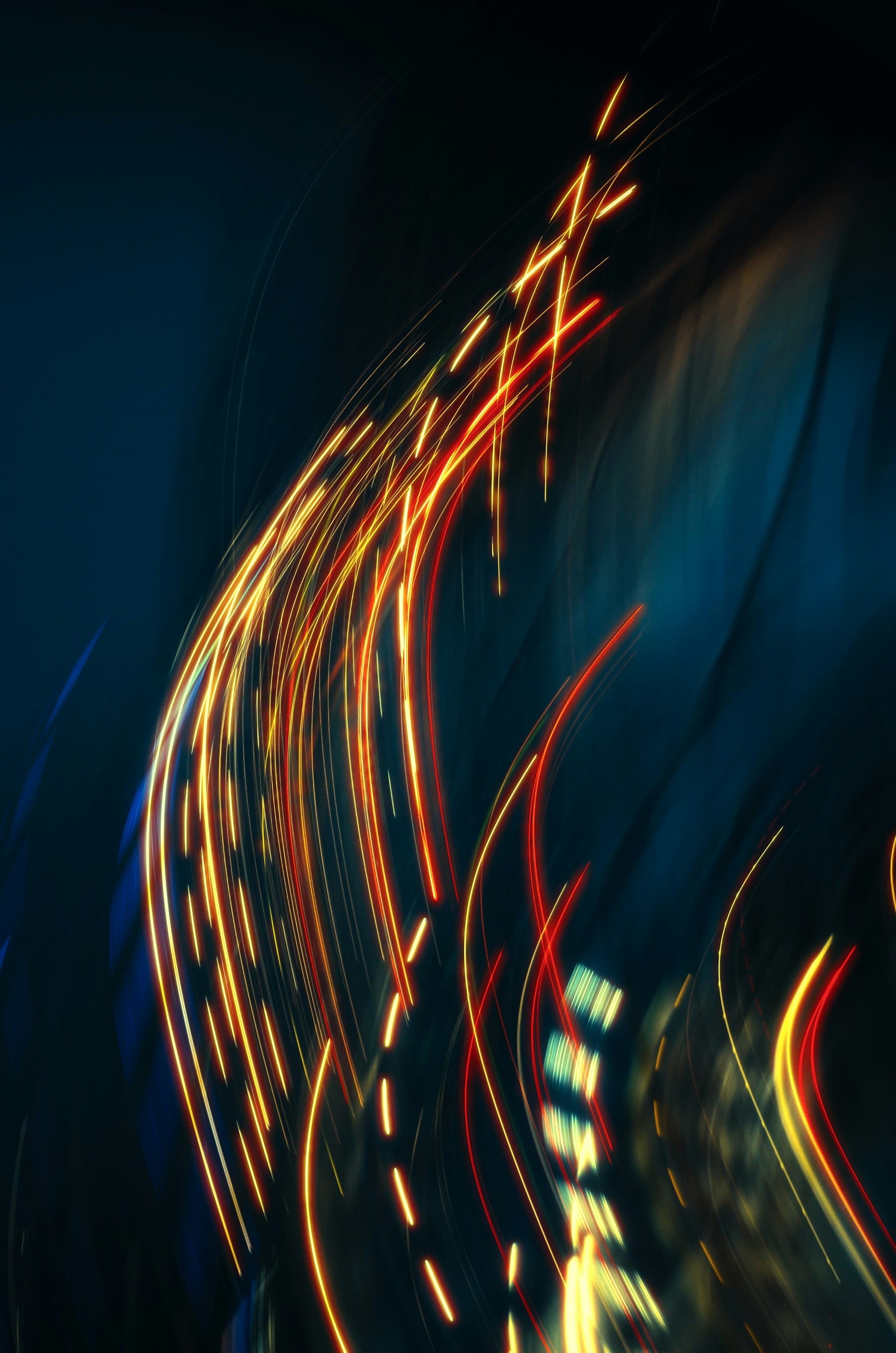 Abstrakte Langzeitbelichtung mit geschwungenen goldroten Lichtspuren vor dunklem, blau getöntem Hintergrund, Sinnbild für kontinuierlichen Betrieb über Zeit