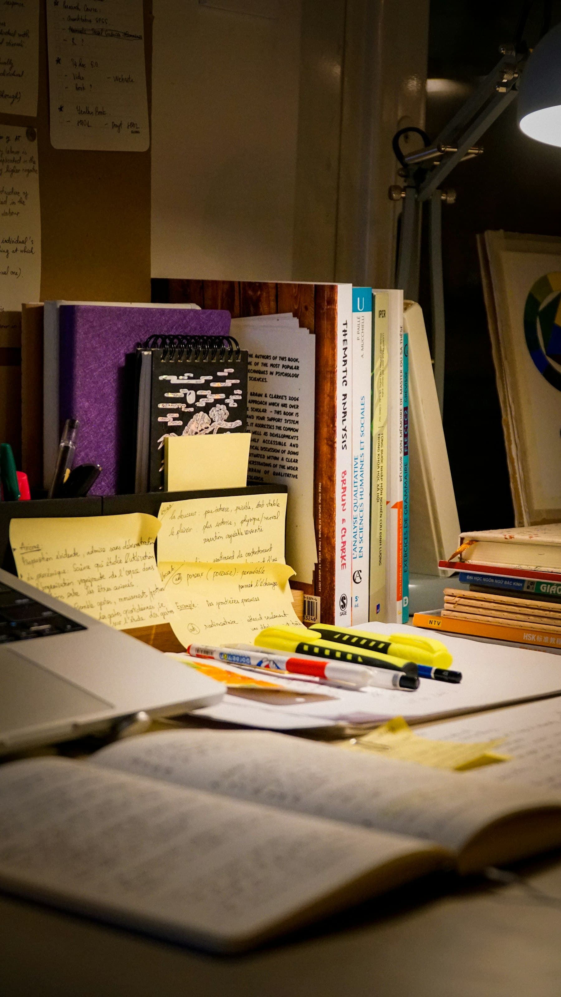 Desk with an open notebook, handwritten sticky notes, and reference books next to a laptop