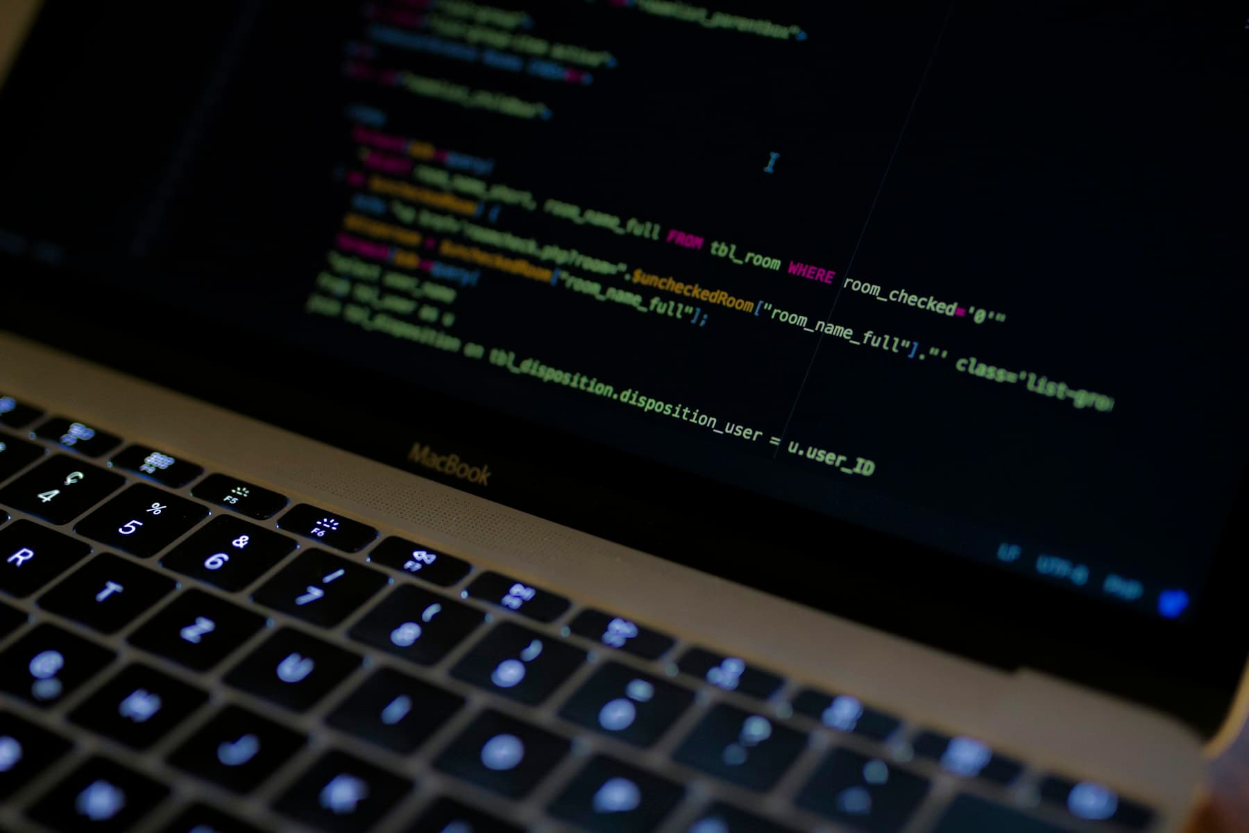 Close-up of a MacBook screen showing a SQL query inside a PHP file in the code editor